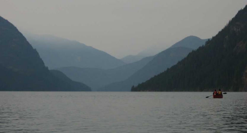 a canoe is paddled on a calm lake with blue mountains in the background